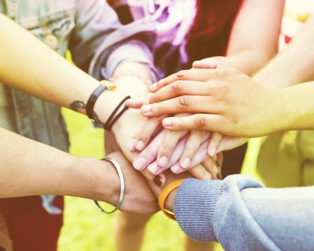 An image of a group of people in a circle with their hands stacked together