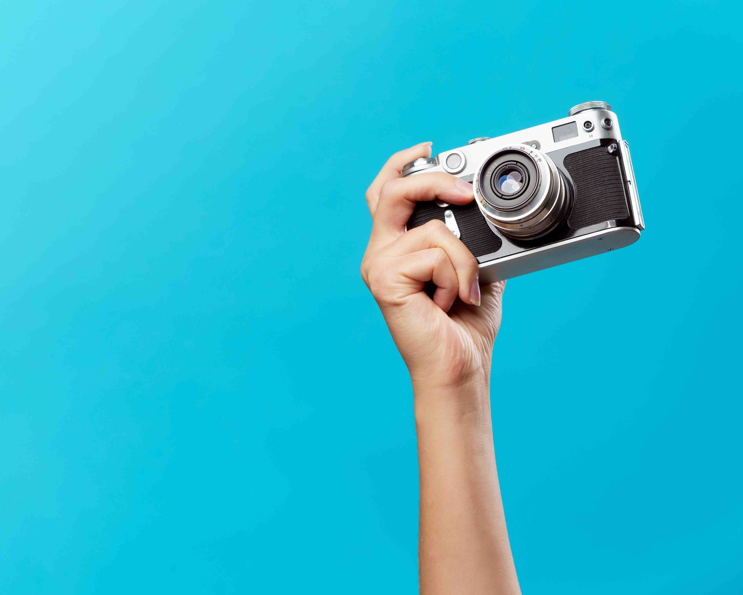 Image of a hand holding a camera up on a blue background